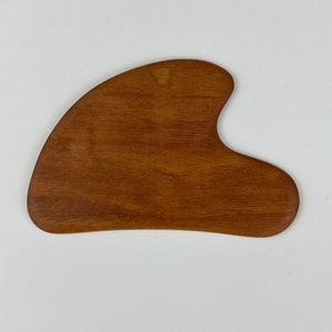 May include: A brown wooden gua sha tool with a heart-shaped design. The tool is used for facial massage and is made of natural wood.