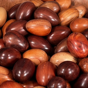 May include: A close-up of a bowl filled with smooth, wooden eggs in various shades of brown, red, and beige.
