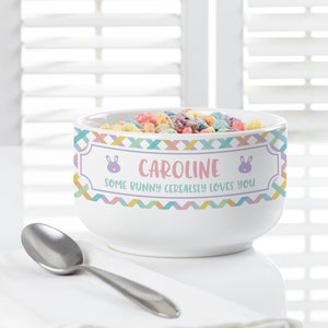 May include: White ceramic bowl with a colorful geometric pattern and the text "Caroline Some Bunny Cerealsly Loves You" with bunny ears on either side of the name. The bowl is filled with colorful cereal.