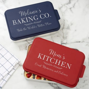 May include: Two rectangular baking pans with lids. The top pan is blue with the text "Melanie's Baking Co. Bake the World a Better Place". The bottom pan is red with the text "Mom's Kitchen Count Memories, not Calories".