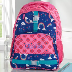 May include: A backpack featuring a dark blue base with a pattern of rainbows, clouds, and flowers, accented by pink floral panels. The front pocket is embroidered with the name Olivia in blue thread and includes teal straps with plastic buckles.