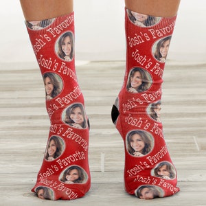 May include: Red socks with a repeating pattern of a woman's face in white ovals, interspersed with the text "Josh's Favorite" in white script. The socks have black heels and toes.