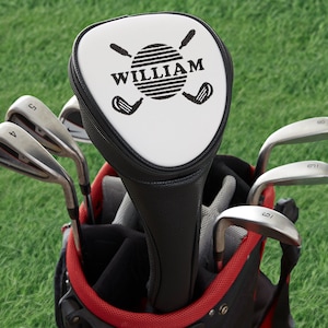 May include: A white golf club head cover with a black golf ball and crossed golf clubs design. The name "WILLIAM" is printed on the cover.