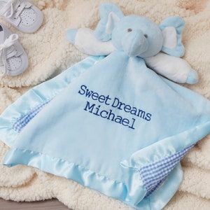 May include: A light blue baby blanket with a blue and white gingham trim and a blue elephant attached. The blanket is embroidered with the text "Sweet Dreams Michael".