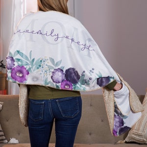 May include: A white fleece throw blanket with a floral design and the text "Mommy" with a heart on either side. The blanket has a sherpa lining and a pocket on one side.