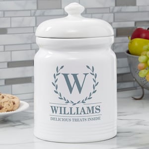 May include: White ceramic cookie jar with a blue and white wreath design and the name "WILLIAMS" and the text "DELICIOUS TREATS INSIDE".