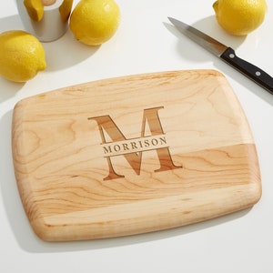 May include: A rectangular wooden cutting board with a rounded edge. The board is engraved with a large letter "M" and the name "MORRISON" below it.