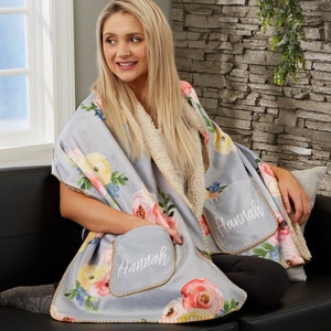 May include: A soft, gray fleece throw blanket with a floral print and two pockets. The pockets are embroidered with the name "Hannah".