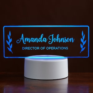 May include: A blue illuminated acrylic desk sign with the text "Amanda Johnson, Director of Operations" and leafy branch designs on either side.