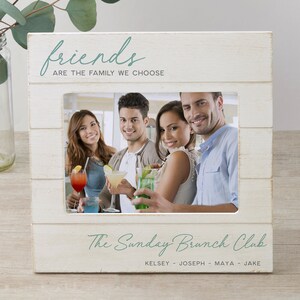 K&ouml;nnte beinhalten: Wei&szlig;er Holzbildrahmen mit einem Foto von vier Freunden, die Getr&auml;nke halten. Der Rahmen tr&auml;gt den Text "friends are the family we choose" oben und "The Sunday Brunch Club Kelsey - Joseph - Maya - Jake" unten.