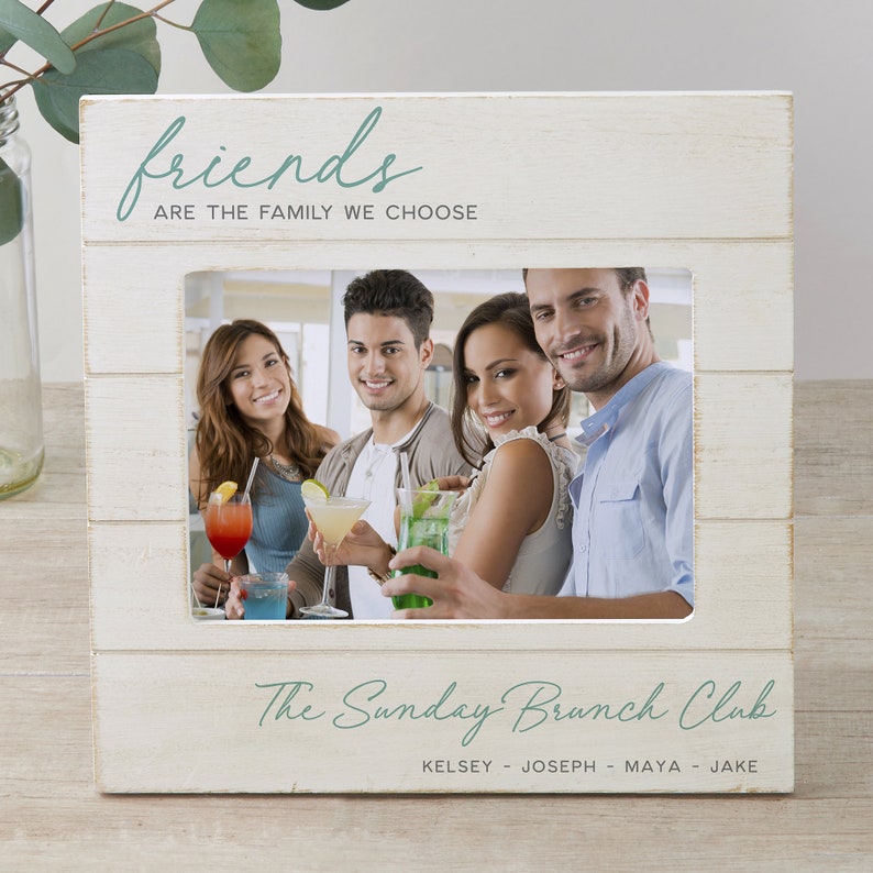 K&ouml;nnte beinhalten: Wei&szlig;er Holzbildrahmen mit einem Foto von vier Freunden, die Getr&auml;nke halten. Der Rahmen tr&auml;gt den Text "friends are the family we choose" oben und "The Sunday Brunch Club Kelsey - Joseph - Maya - Jake" unten.