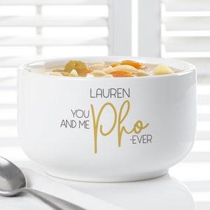 K&ouml;nnte beinhalten: Wei&szlig;er Keramik-Suppenteller gef&uuml;llt mit Suppe, mit Karotten, Nudeln und Gem&uuml;se. Die Sch&uuml;ssel tr&auml;gt den Text "LAUREN, YOU AND ME Pho -EVER" in gold- und schwarzer Schrift. Ein silberner L&ouml;ffel ist sichtbar.