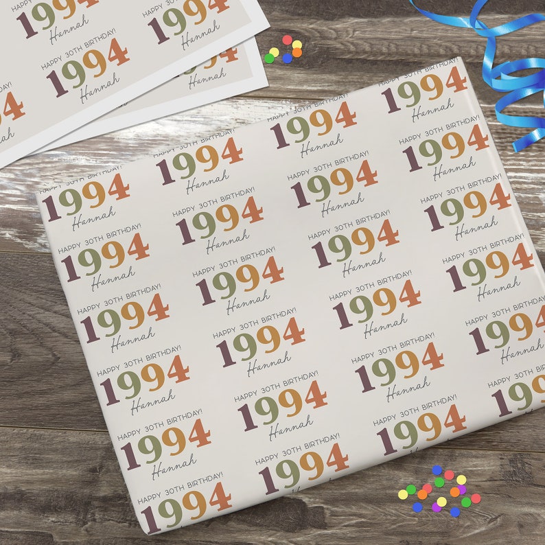 May include: White wrapping paper with a repeating pattern of the year "1994", the name "Hannah", and "Happy 30th Birthday!" in various colors. Confetti and a blue ribbon are scattered around.