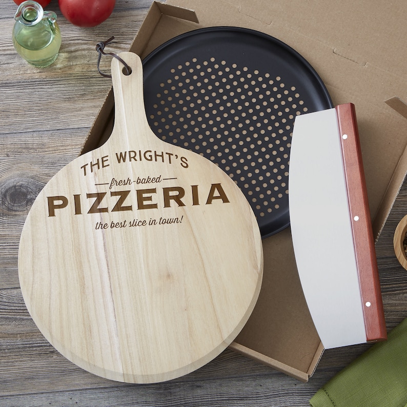 May include: A round wooden pizza peel with a handle and leather cord, engraved with THE WRIGHT'S fresh-baked PIZZERIA the best slice in town!, a black perforated metal pizza pan, and a curved metal pizza cutter with a wooden handle in a box.