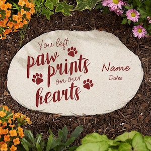 May include: A light-colored stone garden marker with the words "You left paw prints on our hearts" in burgundy script. Paw print icons are also included. Space is available for a name and dates.