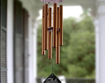 May include: Bronze-colored wind chimes with a wooden top and a decorative diamond-shaped tag. The chimes have multiple cylindrical tubes hanging from the top, creating a melodic sound. The tag features the name "McCarthy" in a stylized font.