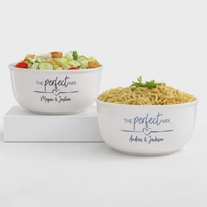 May include: Two white ceramic bowls filled with food, one with salad and the other with noodles. Each bowl has the text "the perfect mix" and a couple's names in blue. The bowls are on a white surface.