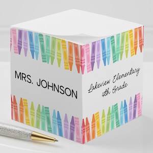 May include: A white cube-shaped notepad with a colorful crayon border. The notepad has the text "MRS. JOHNSON" and "Lakeview Elementary 4th Grade" printed on it.