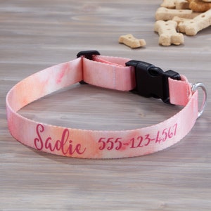 Pu&ograve; includere: Collare rosa per cani con effetto acquerello, con il nome "Sadie" e un numero di telefono in corsivo rosa. Il collare ha una fibbia in plastica nera e un anello a D in metallo argentato.