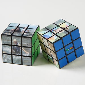 May include: Two Rubik's Cubes with custom photos on each square. One cube has green sides, the other blue. The blue cube has the Rubik's logo. The photos appear to be of people in a natural setting.