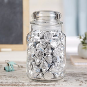 May include: A clear glass jar with a lid filled with silver foil-wrapped chocolate kisses.