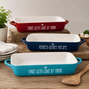 May include: Three rectangular ceramic baking dishes in red, navy blue, and teal. Each dish has a white interior and handles. Text on the dishes reads "MADE WITH LOVE BY NANA" and "Renee's Secret Recipe".