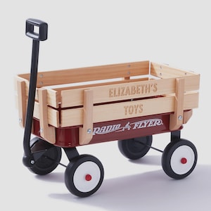 May include: A red Radio Flyer wagon with wooden sides. The wagon has black wheels with white rims and red center caps. The words "ELIZABETH'S TOYS" are engraved on the side. A black handle extends from the front.