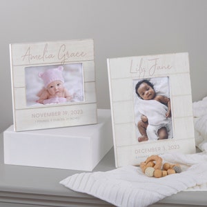 May include: Two white wooden picture frames with a white background. The frames have a rustic wood plank design. The top frame has the name "Amelia Grace" and the date "November 19, 2023" with the birth weight and length. The bottom frame has the name "Lily Jane" and the date "December 3, 2023".