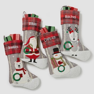 May include: Four personalized Christmas stockings featuring a gray linen-look body with white faux-fur cuffs and red plaid tops. Each stocking displays a unique embroidered character: a polar bear, Santa Claus, a snowman, and a reindeer.