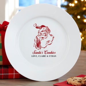May include: White ceramic plate with a red Santa Claus graphic and the text "Santa's Cookies LOVE, CLAIRE & ETHAN". The plate is round and has a wide rim. A festive holiday item.