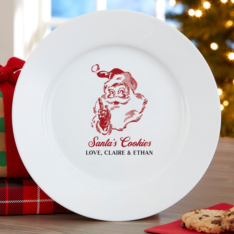 May include: White ceramic plate with a red Santa Claus graphic and the text "Santa's Cookies LOVE, CLAIRE & ETHAN". The plate is round and has a wide rim. A festive holiday item.