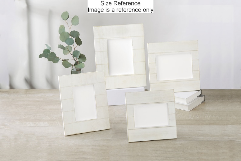 May include: Four white wooden picture frames of different sizes, arranged on a light wood surface. The frames have a rustic, weathered look and are ideal for displaying photos or artwork.