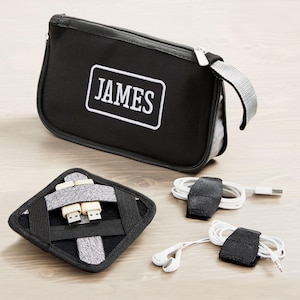 May include: Black travel organizer with the name "JAMES" in white lettering. Includes a zippered pouch, a square organizer with USB cables, and two cable organizers with white cords and earbuds.