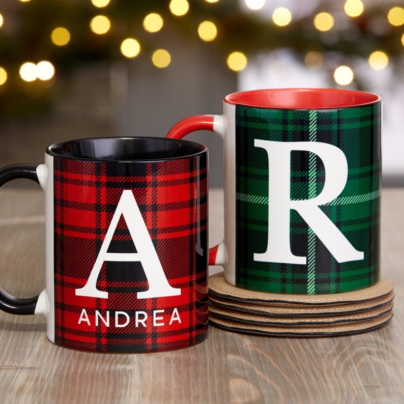 Puede incluir: Dos tazas de cer&aacute;mica con inicial y nombre personalizados. La taza de la izquierda tiene un patr&oacute;n de cuadros rojos y negros con la letra "A" y el nombre "Andrea". La taza de la derecha tiene un patr&oacute;n de cuadros verdes y negros con la letra "R".