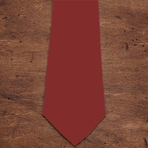 May include: A plain burgundy tie, presented on a wooden surface. The tie is a deep red colour and has a traditional pointed end. The background features a warm-toned wood grain.