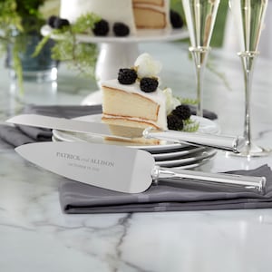 May include: A silver cake knife and server set with the names "Patrick and Allison" and the date "October 19, 2026" engraved on the server. The set is displayed with a slice of cake topped with blackberries and white flowers.