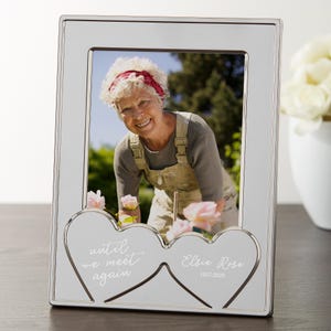 May include: Silver-toned picture frame with a photograph of a smiling woman. The frame has a double-heart cutout at the bottom with the text "until we meet again" and "Elsie Rose 1937-2020".