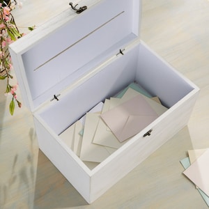 May include: White wooden box with a hinged lid and a slot on the top. The box is open and filled with white and light blue envelopes.