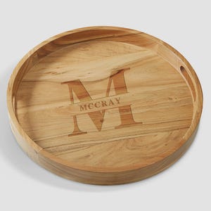 May include: A round wooden serving tray featuring a natural light brown wood grain finish. The center of the tray is engraved with a large capital letter M and the name MCCRAY centered horizontally across the letter in a serif font.