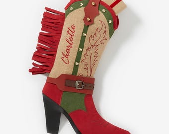 May include: A red and tan Christmas stocking shaped like a cowboy boot. The boot features a red fringe, a green and tan upper, and the name "Charlotte" embroidered in red. A small gift is tucked inside.