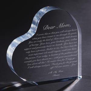 May include: A heart-shaped clear glass plaque featuring an engraved message that begins with Dear Mom, and ends with All My Love, Hanna. The text expresses gratitude and affection, etched into the smooth, transparent surface of the glass object.