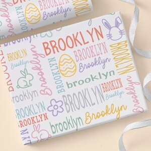 May include: White wrapping paper with a repeating pattern of the name "Brooklyn" in various colors and sizes. The pattern also includes Easter-themed images such as bunnies, eggs, and flowers.