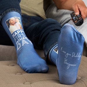 May include: A pair of blue socks with a photo of a father and child on one sock and the text "Happy First Father's Day" on the other sock. The other sock has the text "Love you Daddy Benjamin" written on it.