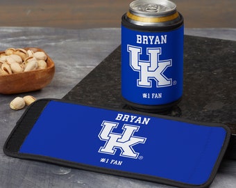 May include: A blue can cooler and a matching rectangular drink holder with the text "BRYAN" and "#1 FAN" in white. The cooler has the UK logo. A can of soda sits in the cooler. The drink holder is on a dark surface.
