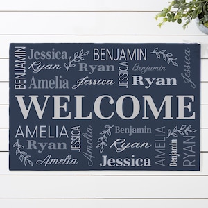 May include: A navy blue welcome mat with the word "WELCOME" in large white letters. The names Amelia, Benjamin, Jessica, and Ryan are repeated in a decorative pattern around the word "WELCOME".