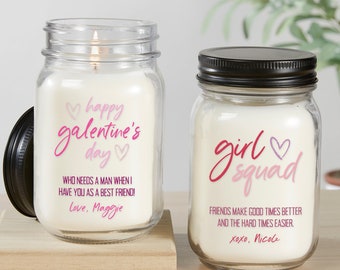 May include: Two glass jar candles with pink and white text. The first candle says "happy galentine's day" with hearts and "Who needs a man when I have you as a best friend! Love, Maggie". The second candle says "girl squad" with a heart and "Friends make good times better and the hard times easier. xoxo, Nicole".