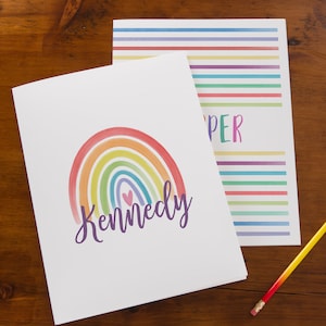 May include: A white folder with a rainbow and the name "Kennedy" in purple text. The folder has a lined sheet of paper with rainbow stripes on the back.