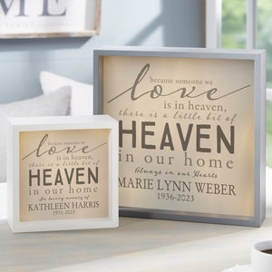 May include: Two memorial shadow boxes with the text "because someone we love is in heaven, there is a little bit of HEAVEN in our home." One box is white, the other is gray. The boxes include names and dates.