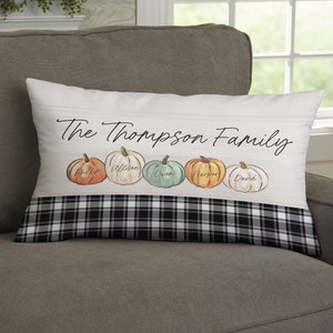May include: Rectangular decorative pillow with the text "The Thompson Family" above five watercolor pumpkins. Each pumpkin has a name written on it. The bottom of the pillow has a black and white plaid pattern.