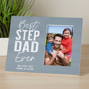 May include: A gray wooden picture frame with the text "Best Step Dad Ever" and "We love you! Emma & Oliver". The frame has a photo of a man with two children.